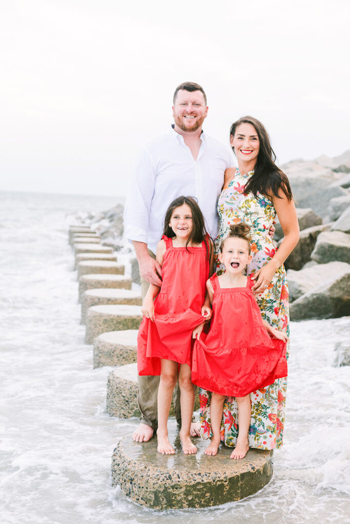 Family standing on rocks above water facing the camera in pops of red color, JCrane Photography, Best family photographer in North Carolina, Top-rated family photographer North Carolina, Outdoor Family Photographer Near Me