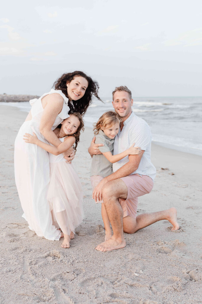 Family embrace on the beach in soft neutral coastal tone clothes full length image, JCrane Photography, Best family photographer in North Carolina, Top-rated family photographer North Carolina, Outdoor Family Photographer Near Me