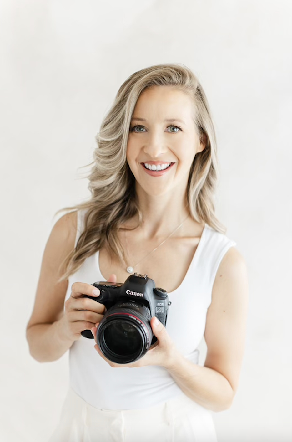 Headshot of Jenna, owner of JCrane Photography, smiling while holding her camera, representing her passion for capturing family, maternity, and newborn moments in Raleigh, North Carolina. JCrane Photography, Raleigh heirloom portraits, Raleigh portrait photography.